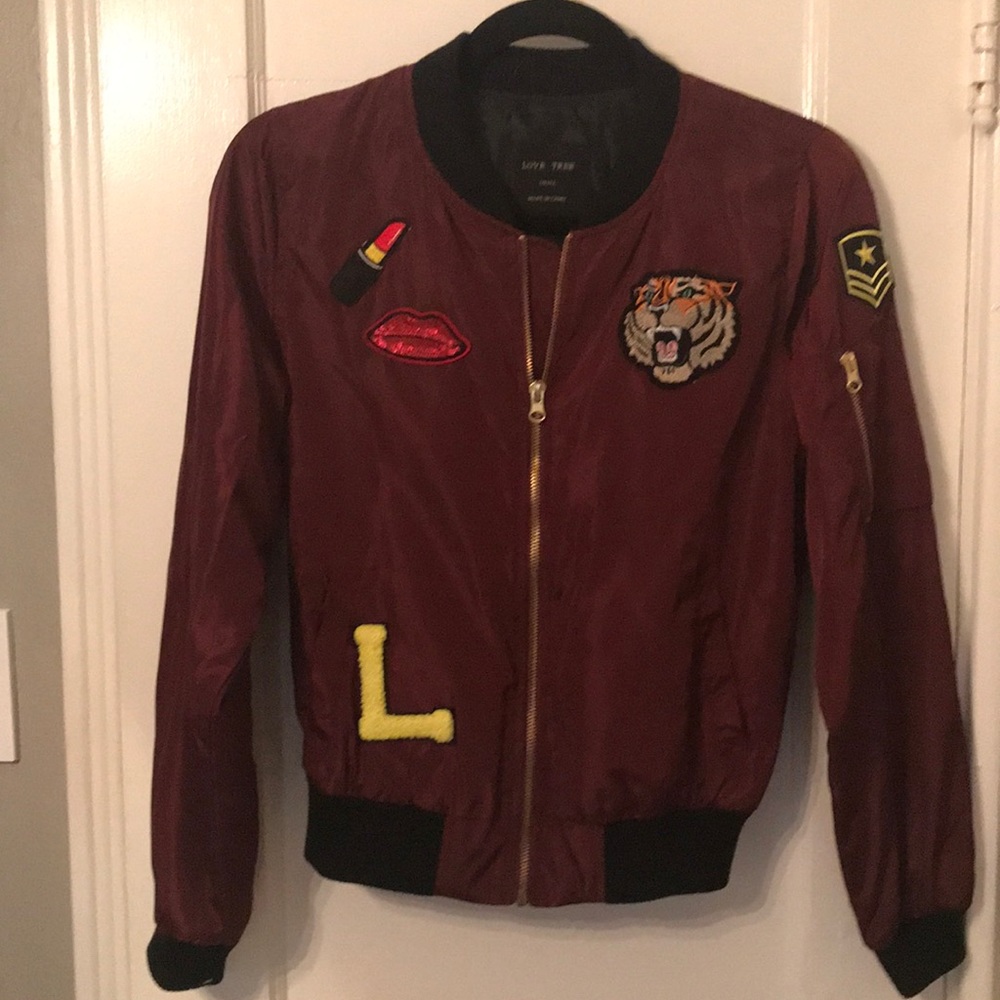 Maroon bomber jacket with various patches.